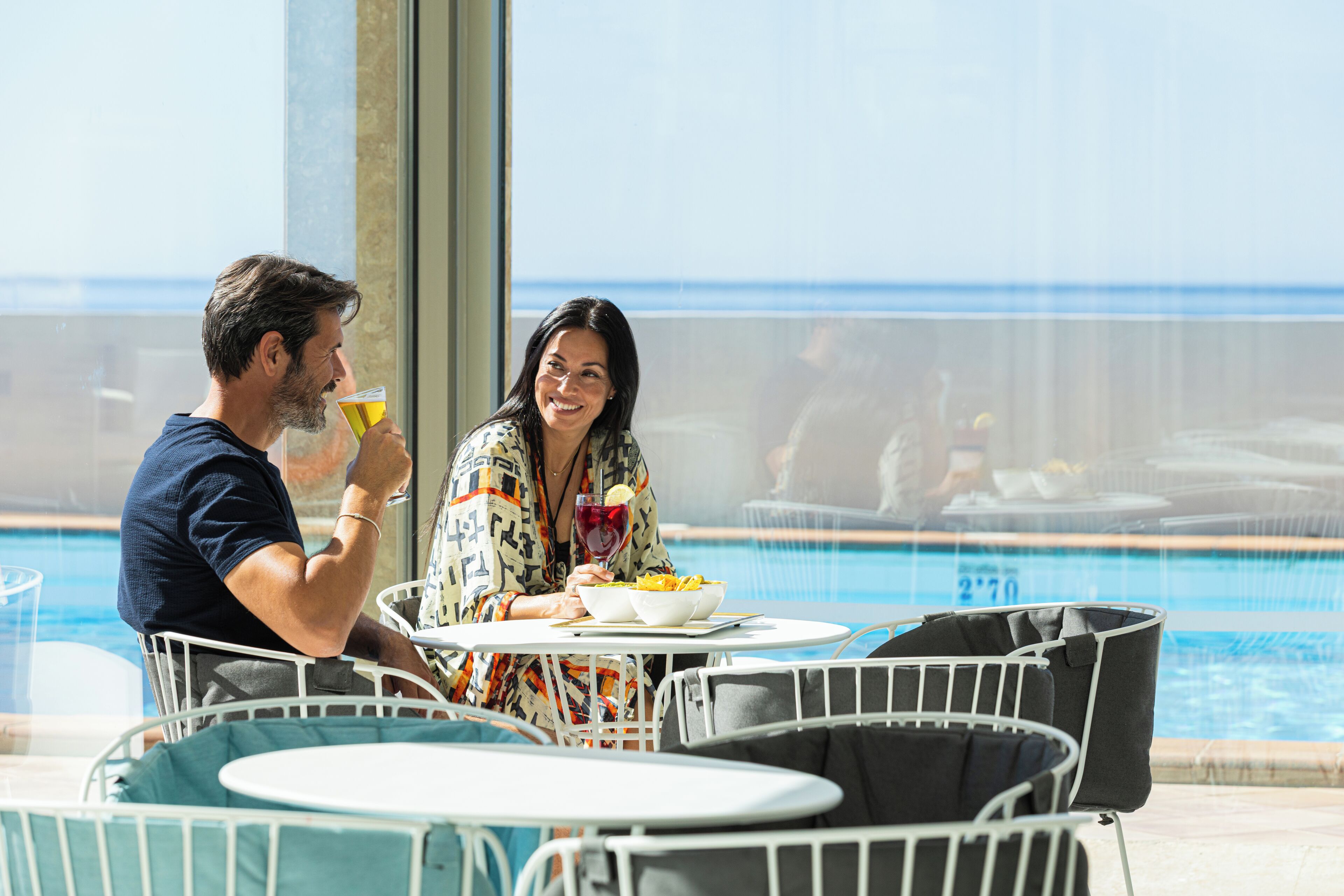 A couple dining by a poolside table with a view of the pool and ocean.