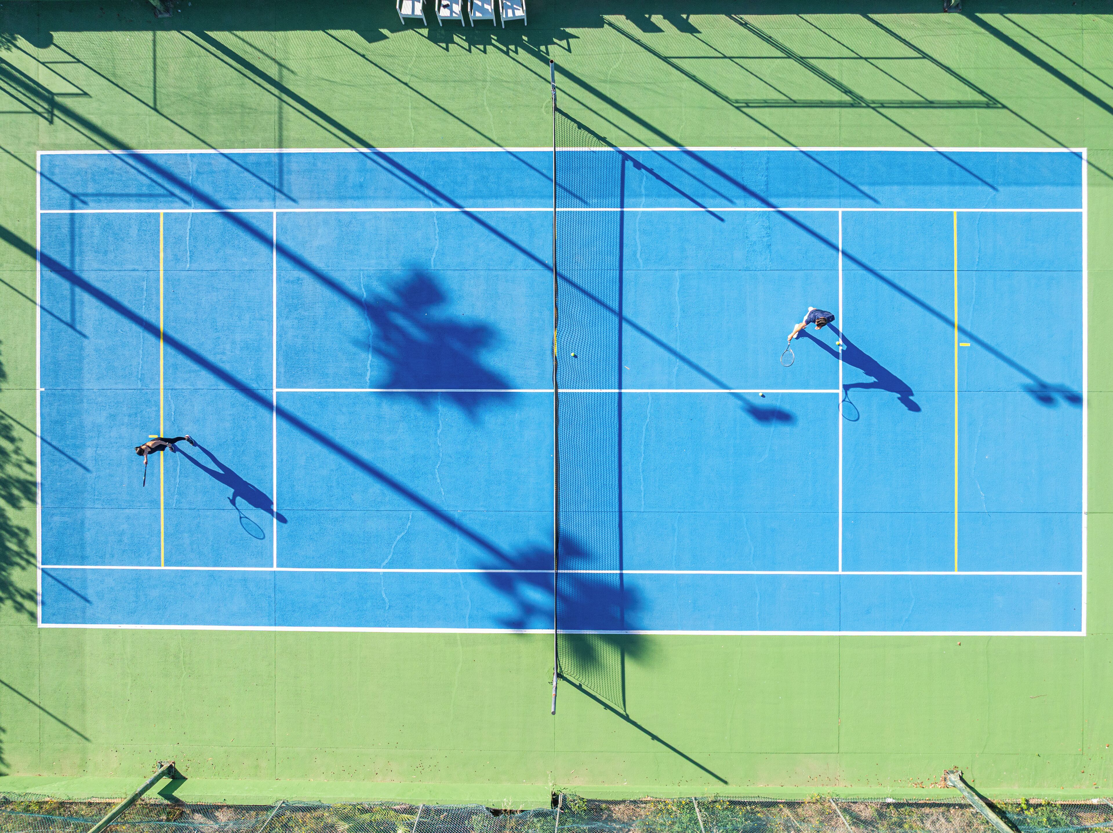 A tennis court with a net in the center, surrounded by a green area.