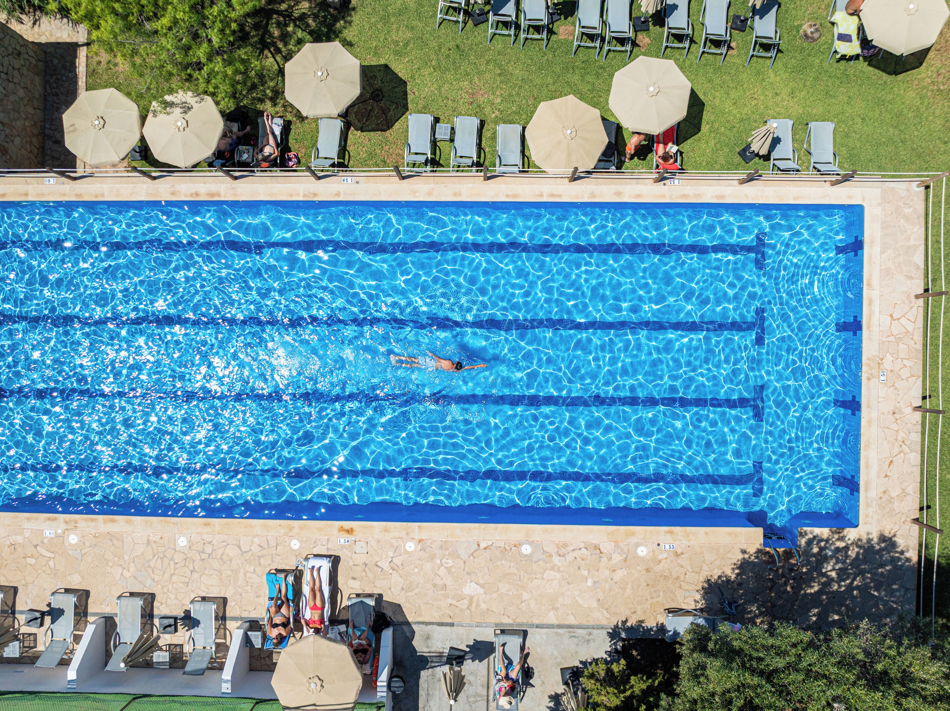 A large rectangular swimming pool with clear blue water, surrounded by lounge chairs and umbrellas.