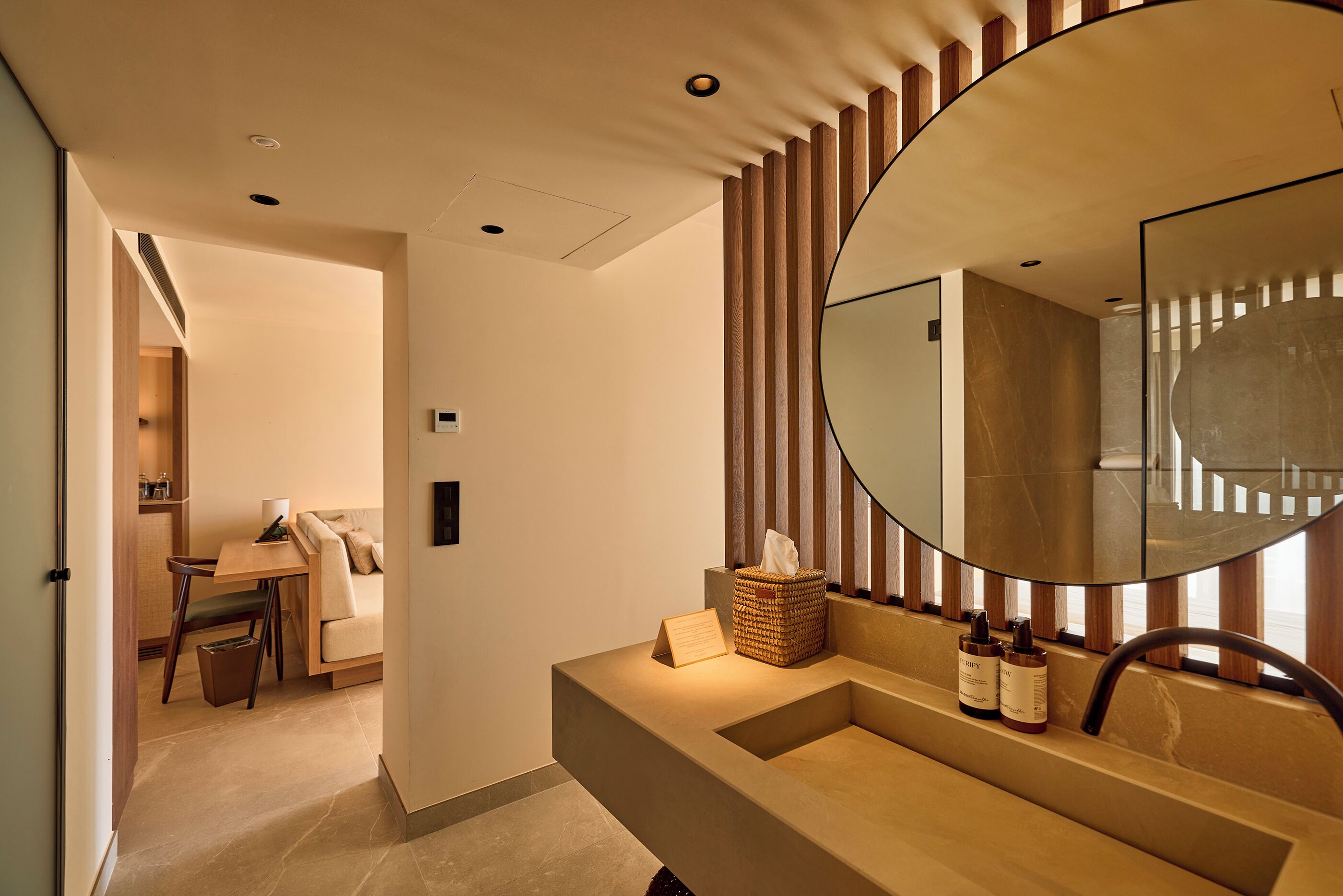 A modern bathroom with a large mirror, a sink, and a small table with a tissue box and toiletries.