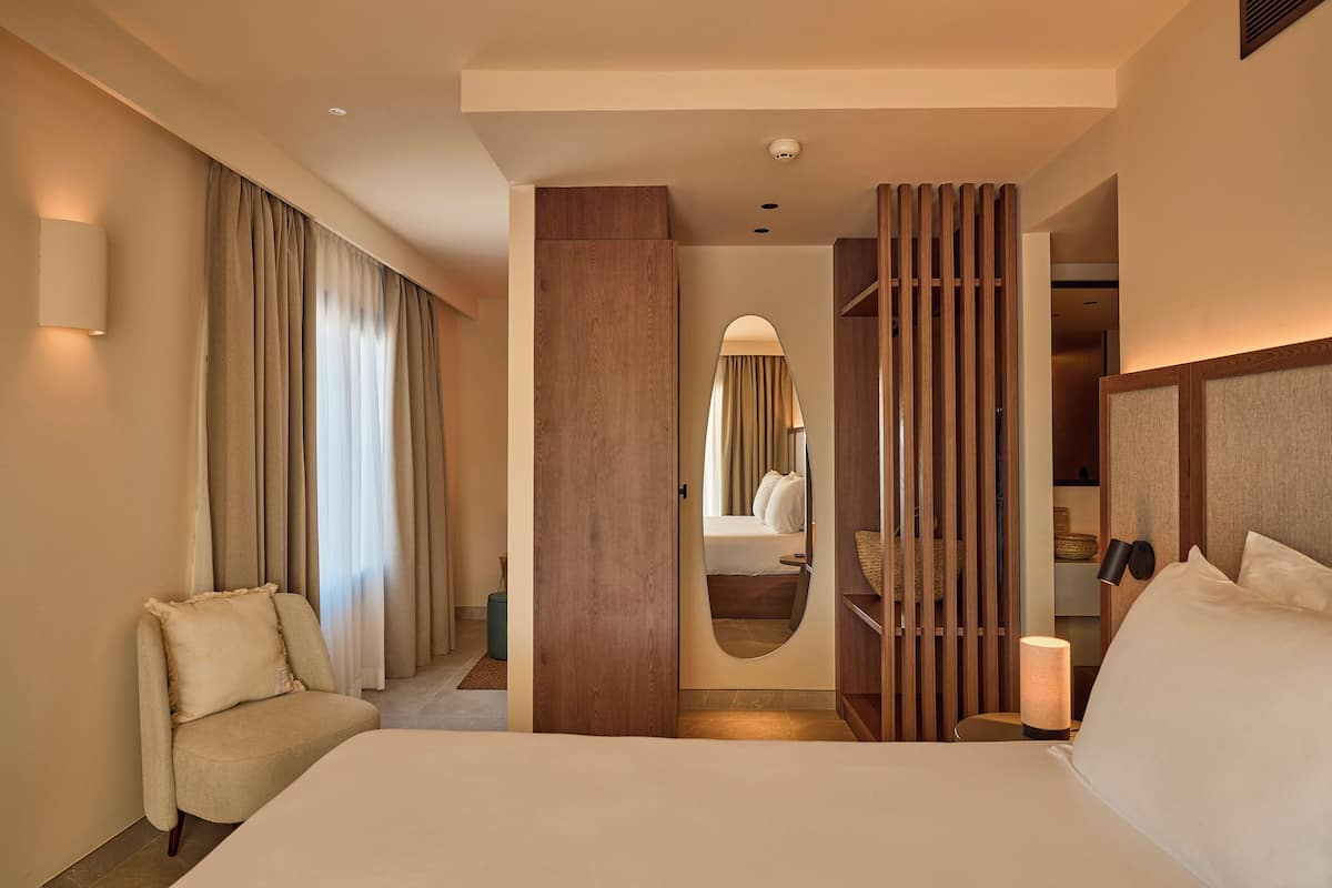 A hotel room with a large bed, a seating area, a wardrobe, and a bathroom visible through a door.