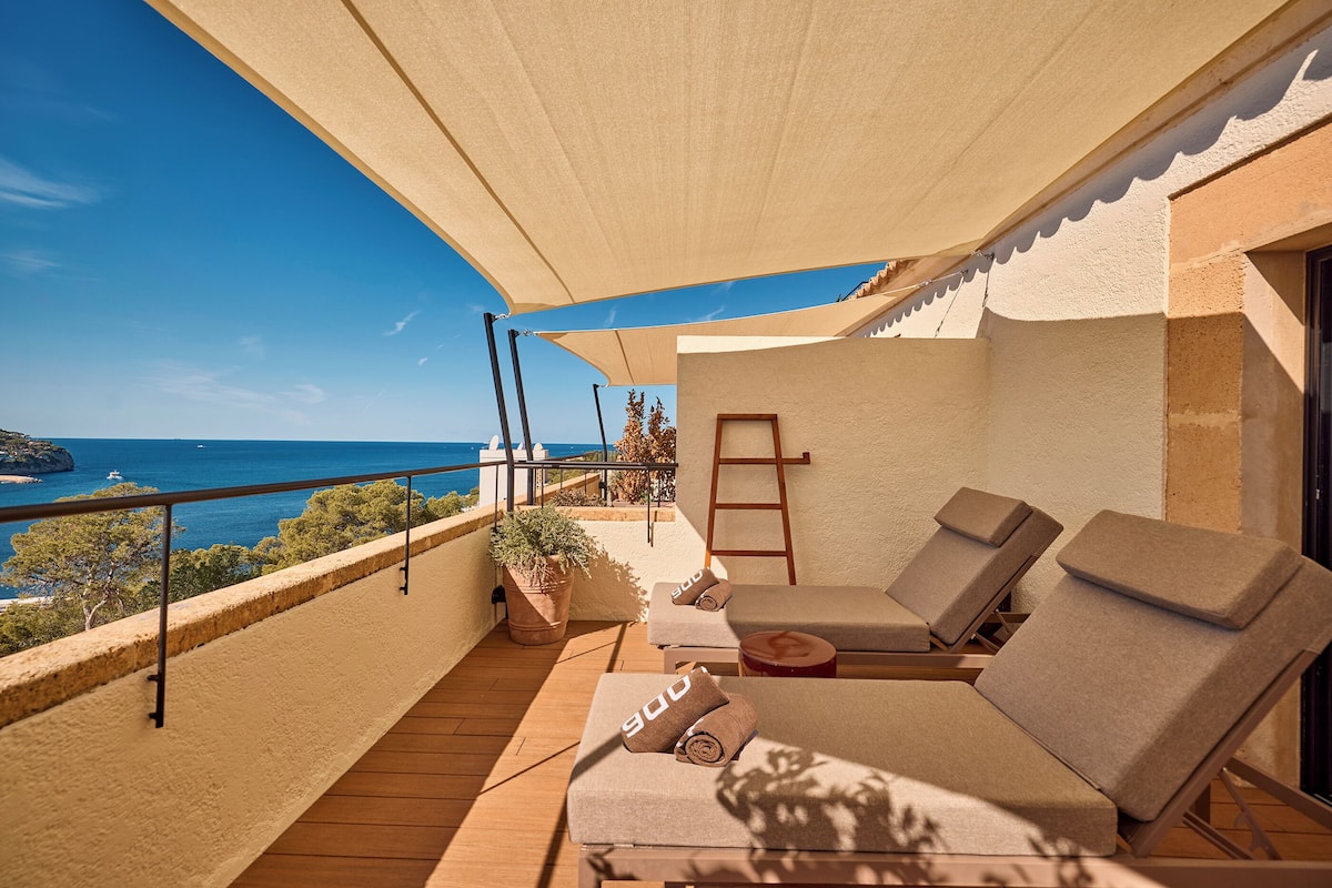 A balcony with a wooden floor, beige cushions, and a view of the sea.