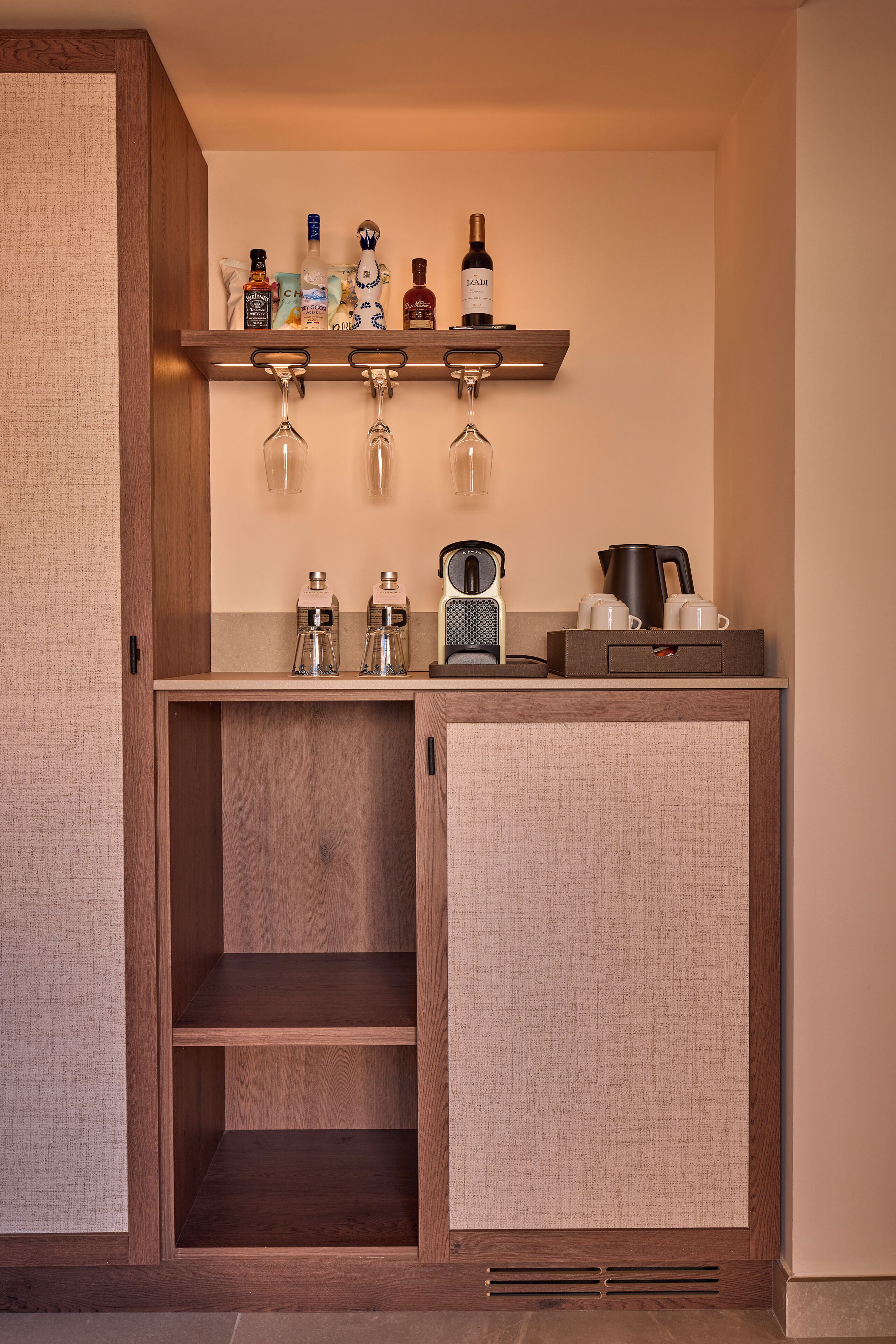 Una kitchenette compacta con un armario de madera, una encimera con cafetera, hervidor y una botella de vino.