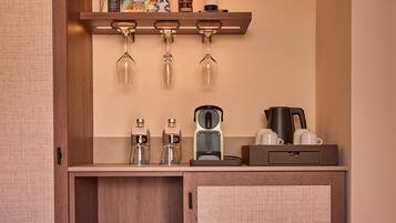 Una kitchenette compacta con un armario de madera, una encimera con cafetera, hervidor y una botella de vino.