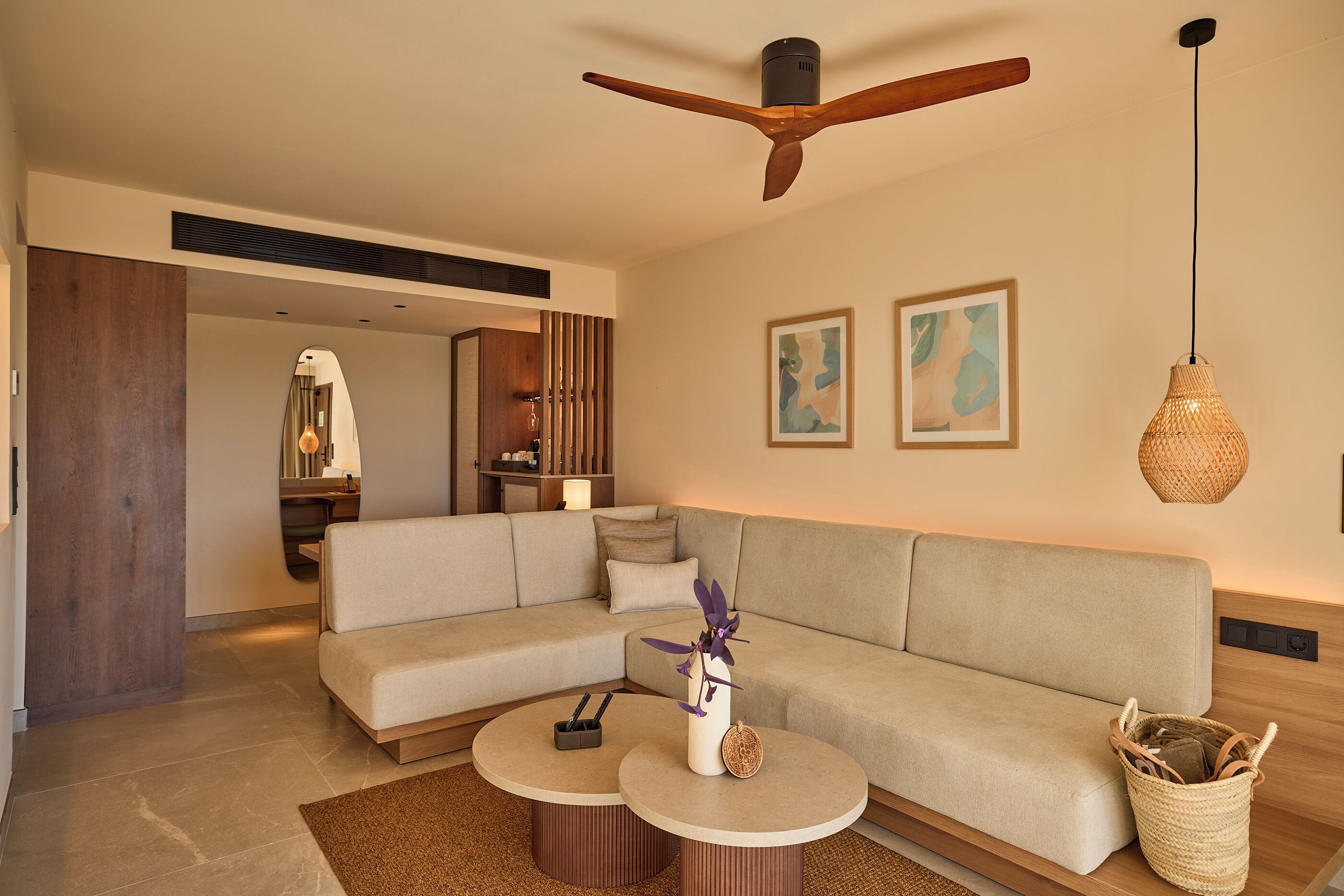 A modern living room with a sectional sofa, two round coffee tables, a ceiling fan, and artwork on the walls.