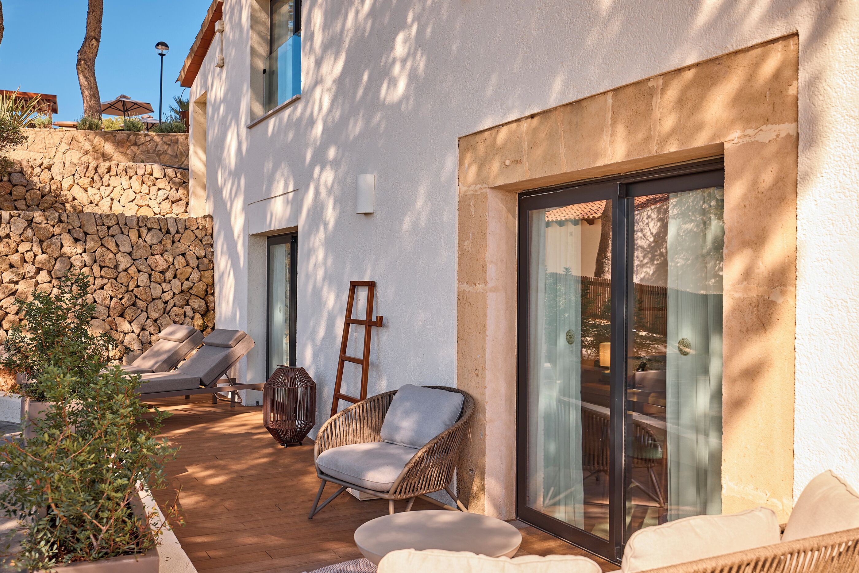 Un patio exterior moderno con sillones de descanso, una silla de mimbre y una pared de piedra.
