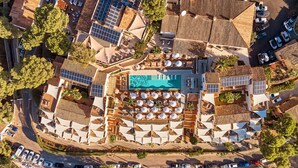 Vue aérienne d’un complexe hôtelier doté d’une piscine centrale, de nombreuses chaises longues et d’un espace de stationnement.