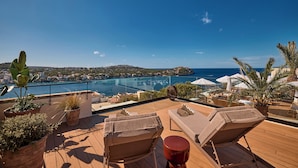Une terrasse sur le toit, aménagée avec des chaises longues, des plantes en pot et offrant une vue sur une ville côtière et la mer.