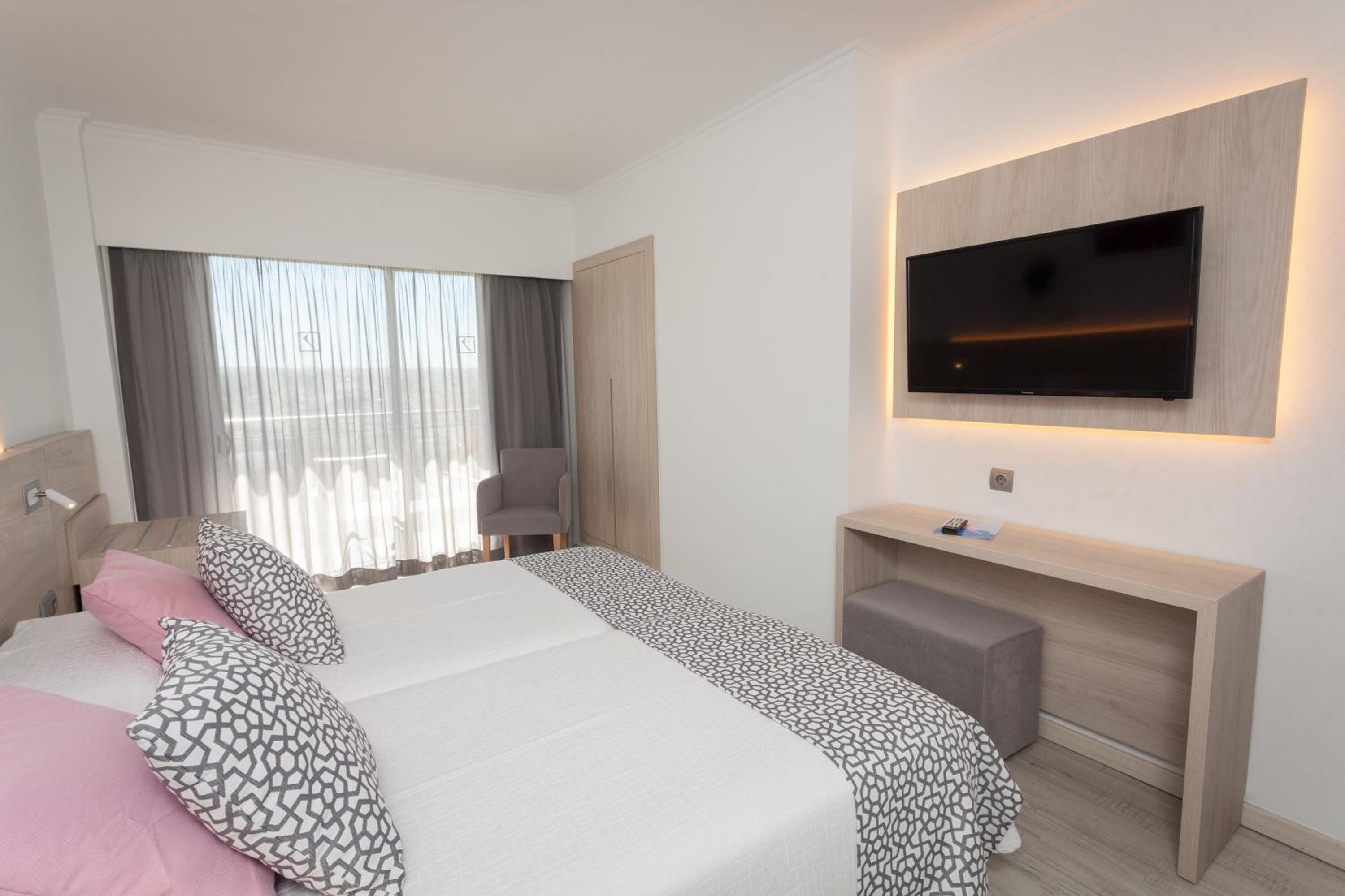 Una habitación de hotel moderna con una cama grande, un televisor montado en la pared, un escritorio y una silla.