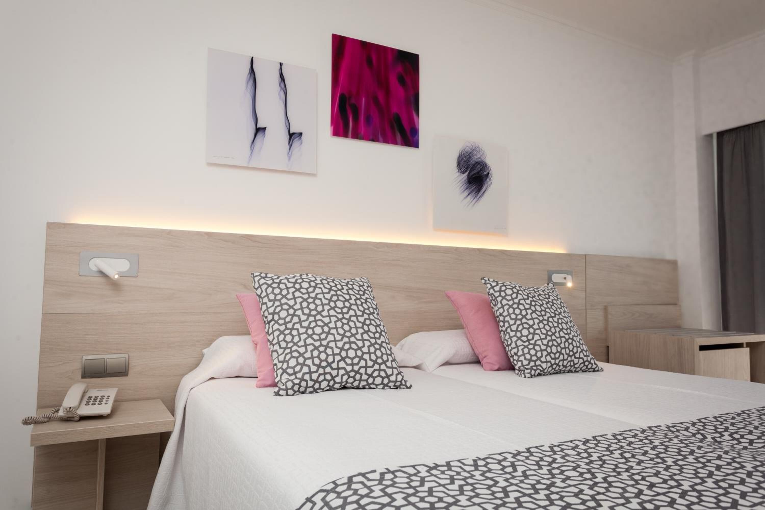 A hotel room with a wooden headboard, a bedside table with a phone, and two beds with patterned pillows.