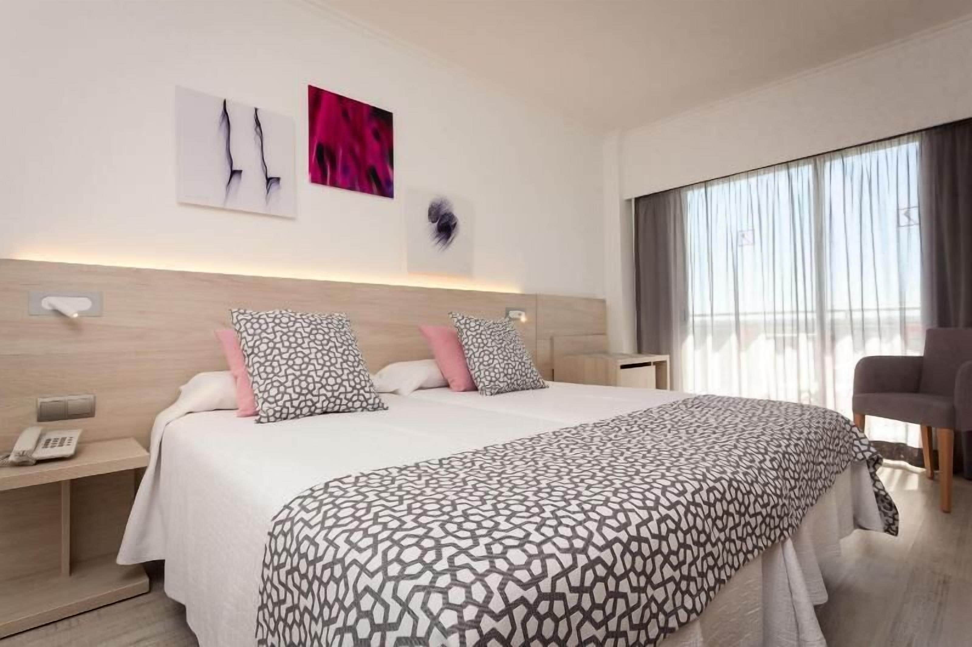A modern hotel room with a large bed, bedside tables, a chair, and a large window with curtains.