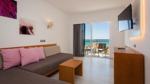 A modern hotel room with a sofa, a wooden coffee table, a TV mounted on the wall, and a balcony with a view of the sea. - Hotel Timor (Palma de Mallorca)