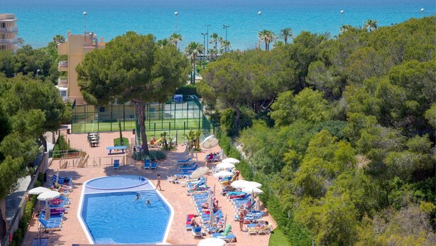 A pool area with a view of the sea, surrounded by trees and buildings. - Hotel Timor (Palma de Mallorca)