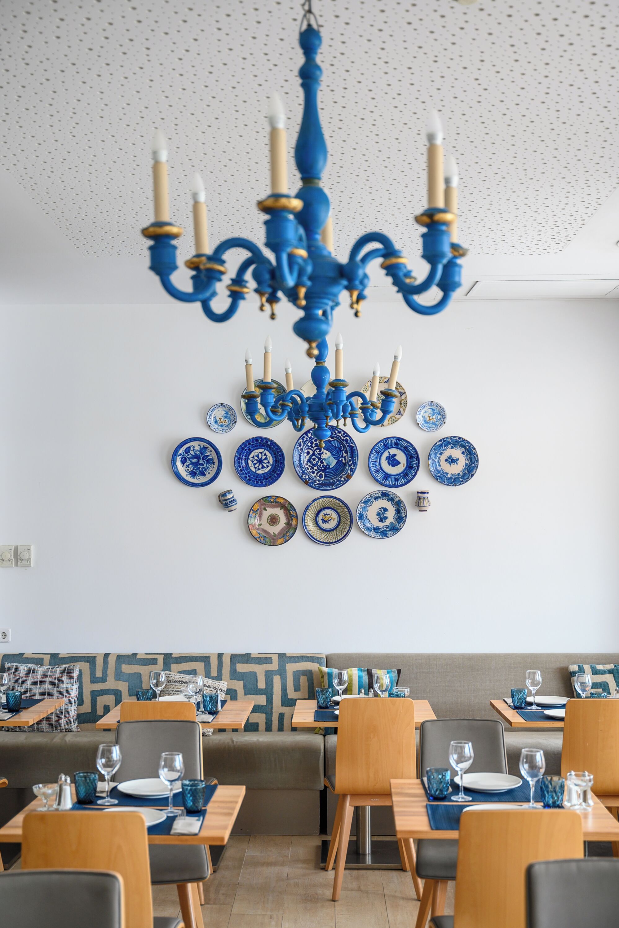 A dining area with blue and white patterned plates, a blue chandelier, and wooden tables and chairs.
