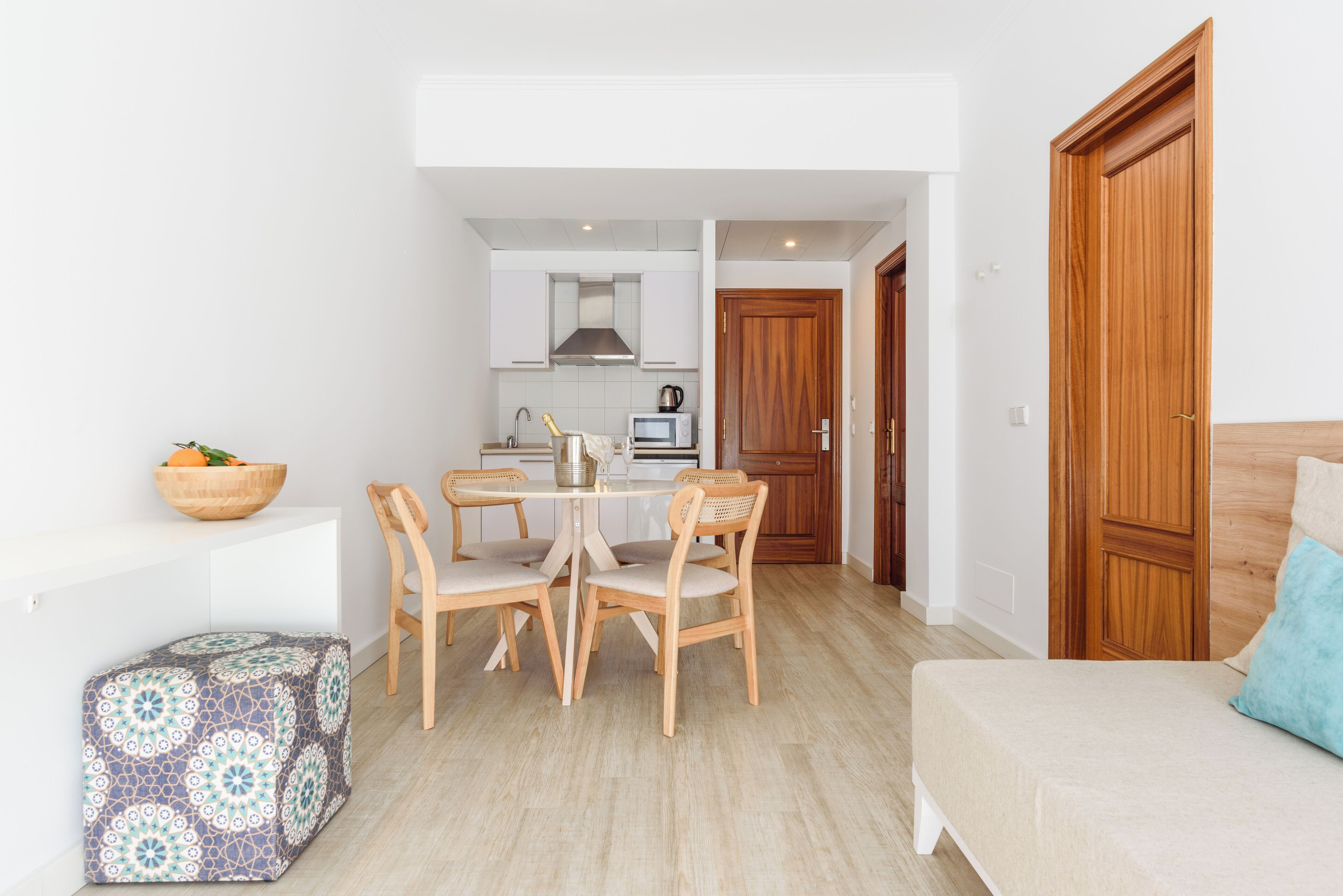 Un espacio habitable compacto con kitchenette, una zona de comedor con mesa y sillas, un sofá y una puerta de madera.