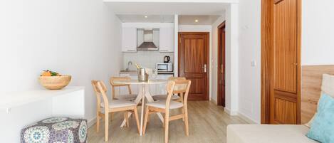Un espacio habitable compacto con kitchenette, una zona de comedor con mesa y sillas, un sofá y una puerta de madera.