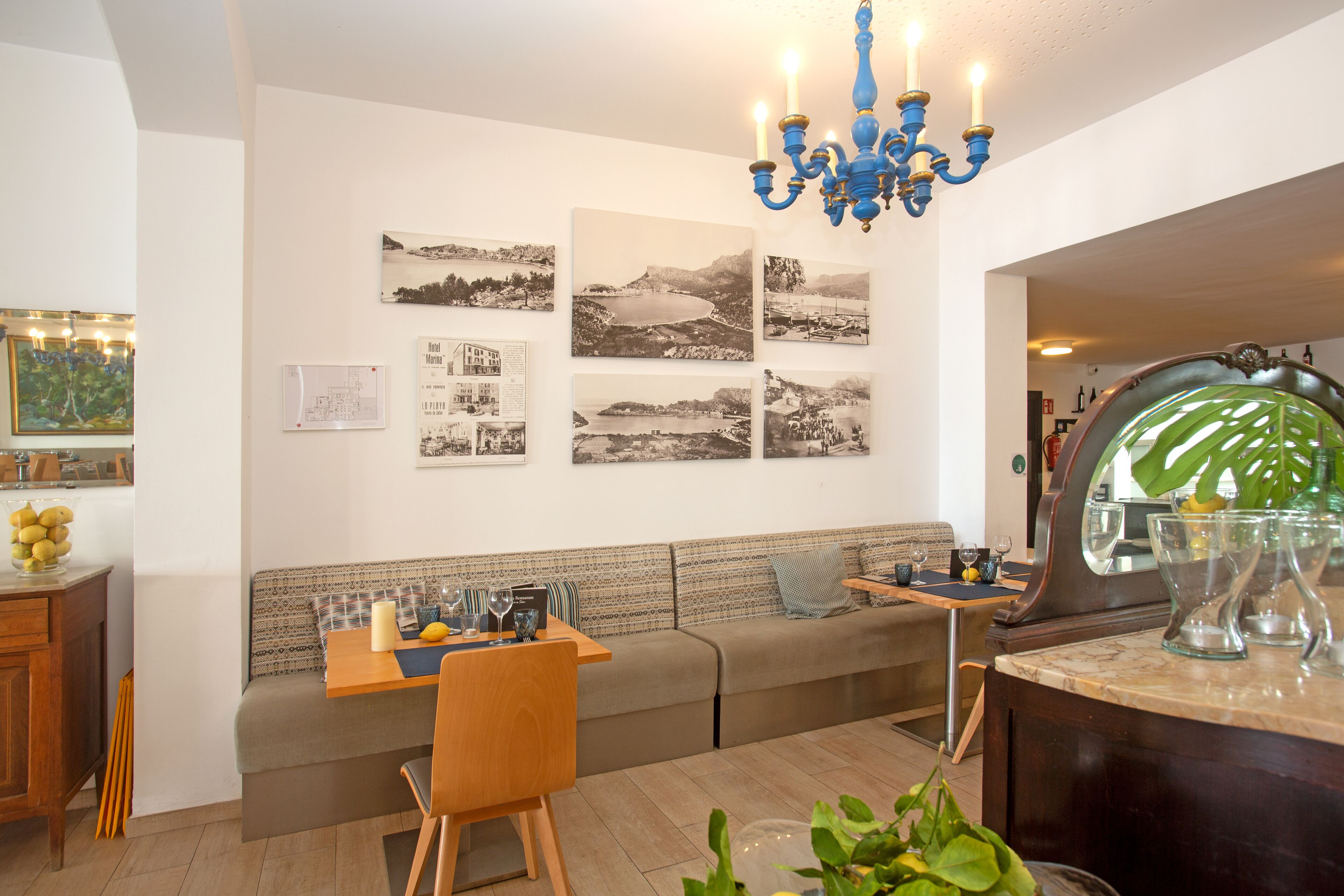 A modern living room with a sofa, dining table, and a chandelier. There are black and white photographs on the wall and a mirror on the right.
