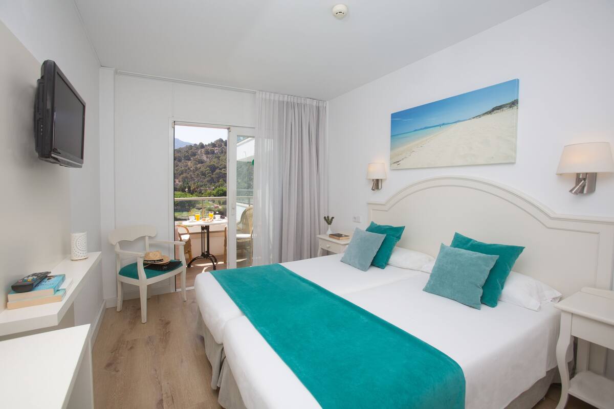 Een hotelkamer met een bed, een bureau, een stoel, een televisie en een schilderij van een strand.