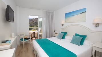 Ett hotellrum med en säng, ett skrivbord, en stol, en tv och en tavla som föreställer en strand.