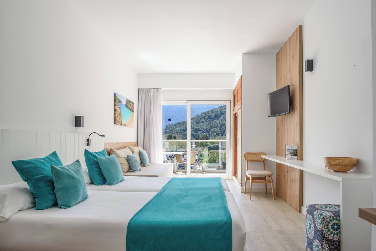 Een moderne hotelkamer met twee bedden, een televisie, een balkon met uitzicht op de bergen en een houten dressoir.