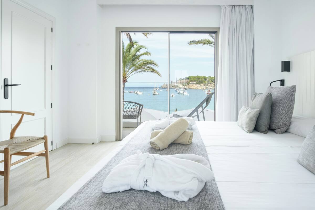 Een slaapkamer met een bed, een stoel, een handdoek en uitzicht op zee.