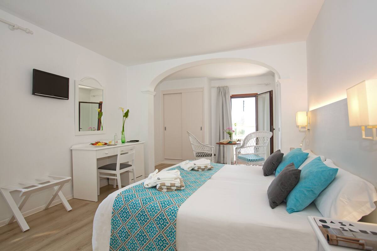 Hotelkamer met een bed, bureau, stoel, televisie en een badkamer zichtbaar door een boog.