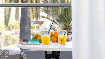 A balcony with a table holding fruit and drinks, a striped towel, and a view of palm trees.