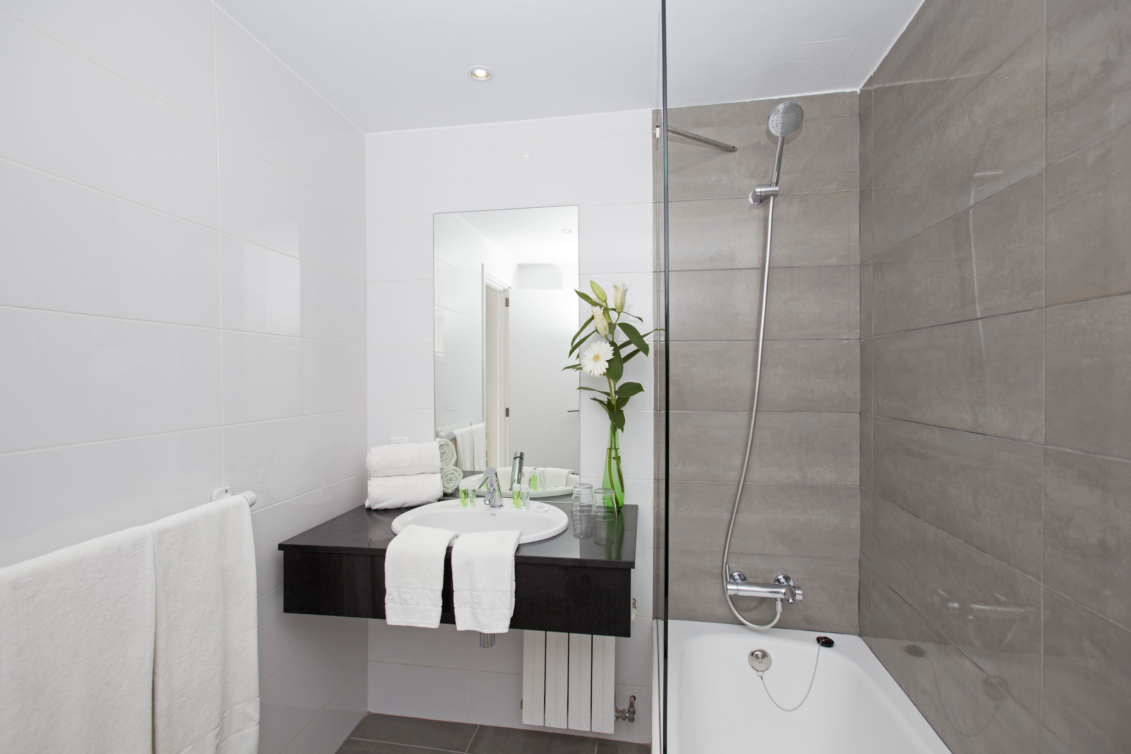 Une salle de bain moderne avec une douche à parois de verre, un lavabo sur un plan de toilette noir et un porte-serviettes blanc.