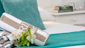 A neatly made bed with a teal bedspread, a rolled towel, and a bouquet of flowers.