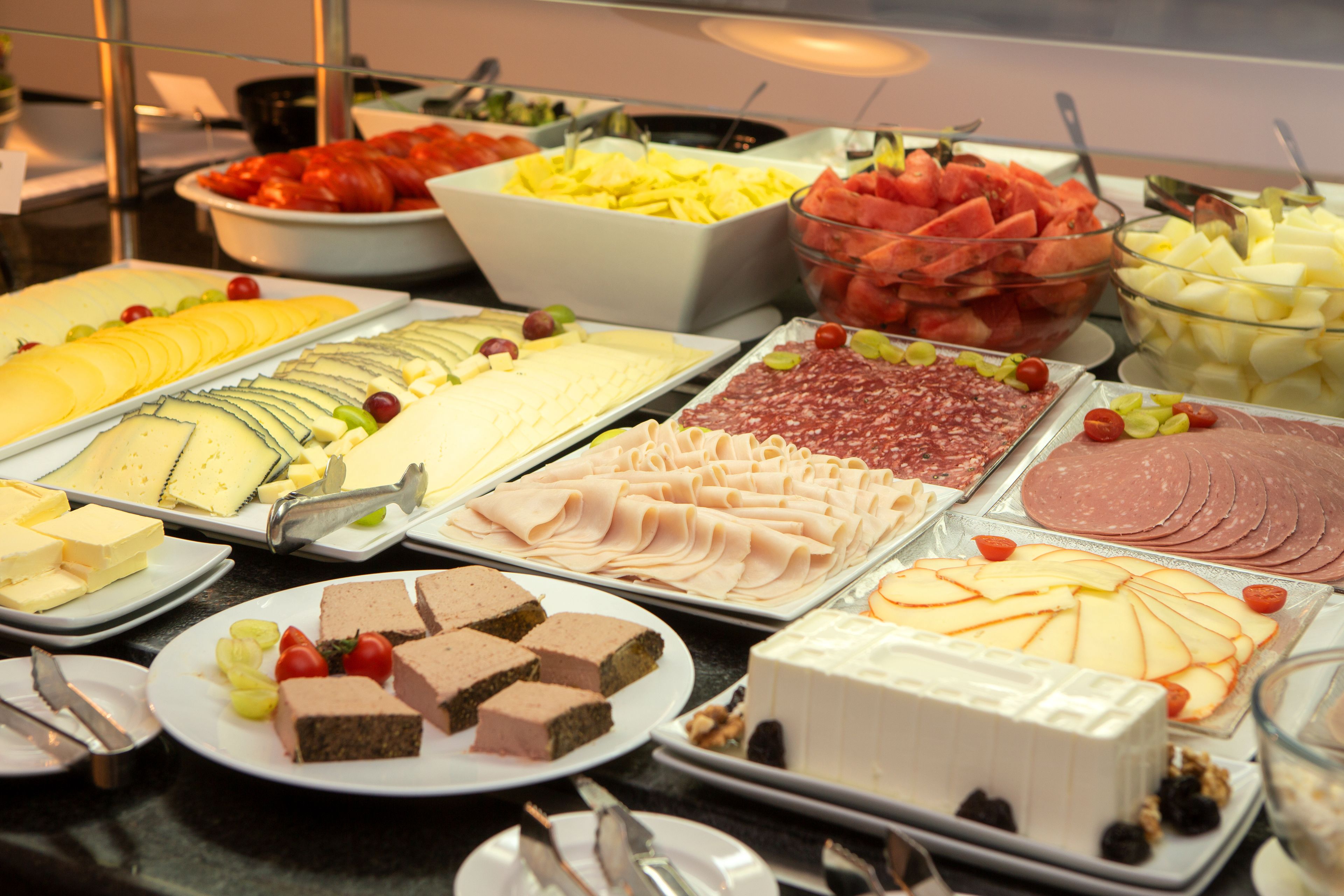 A buffet with various food items including cheese, meats, fruits, and desserts.