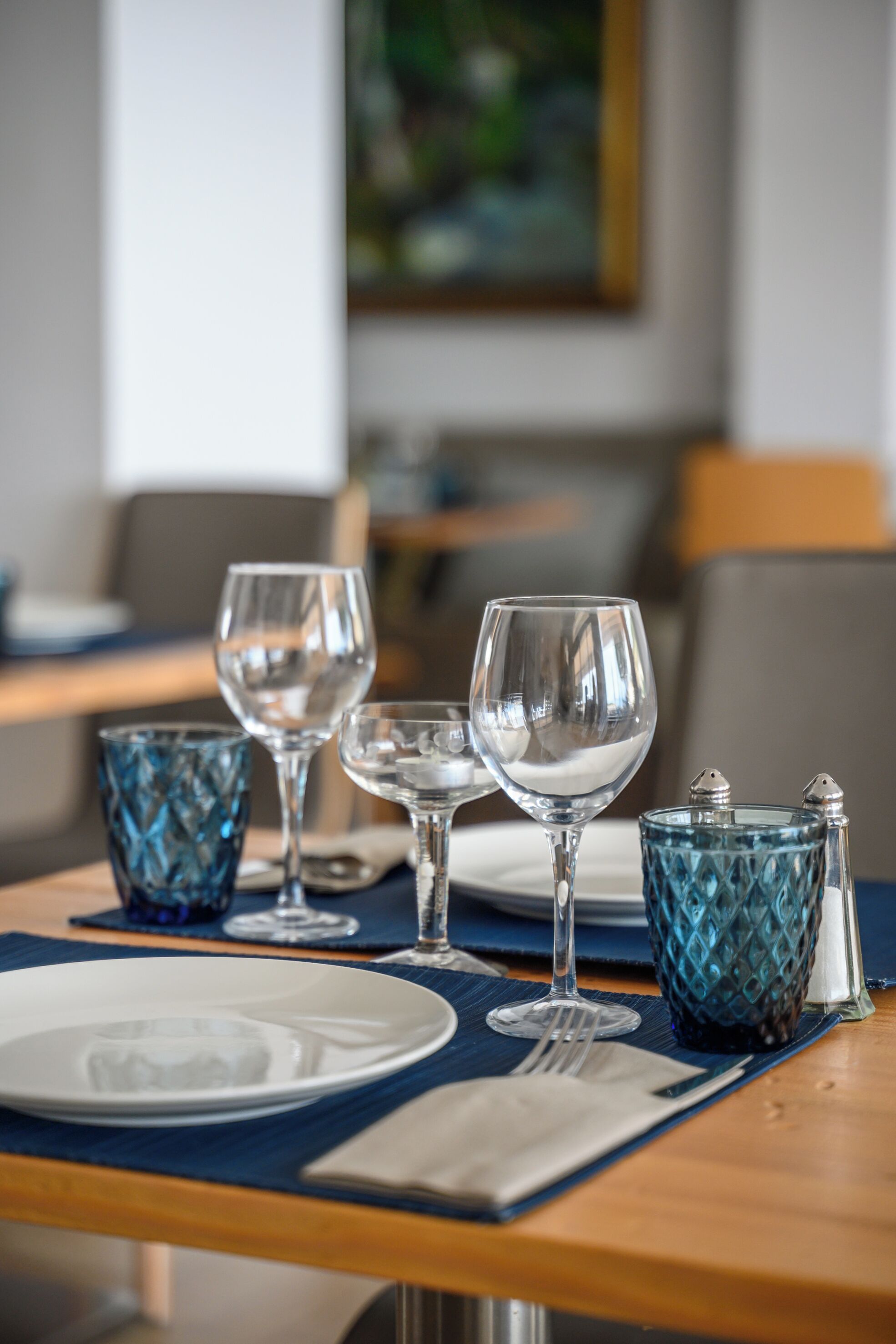 A dining table set with clear glassware, a blue textured glass, and a salt and pepper set.