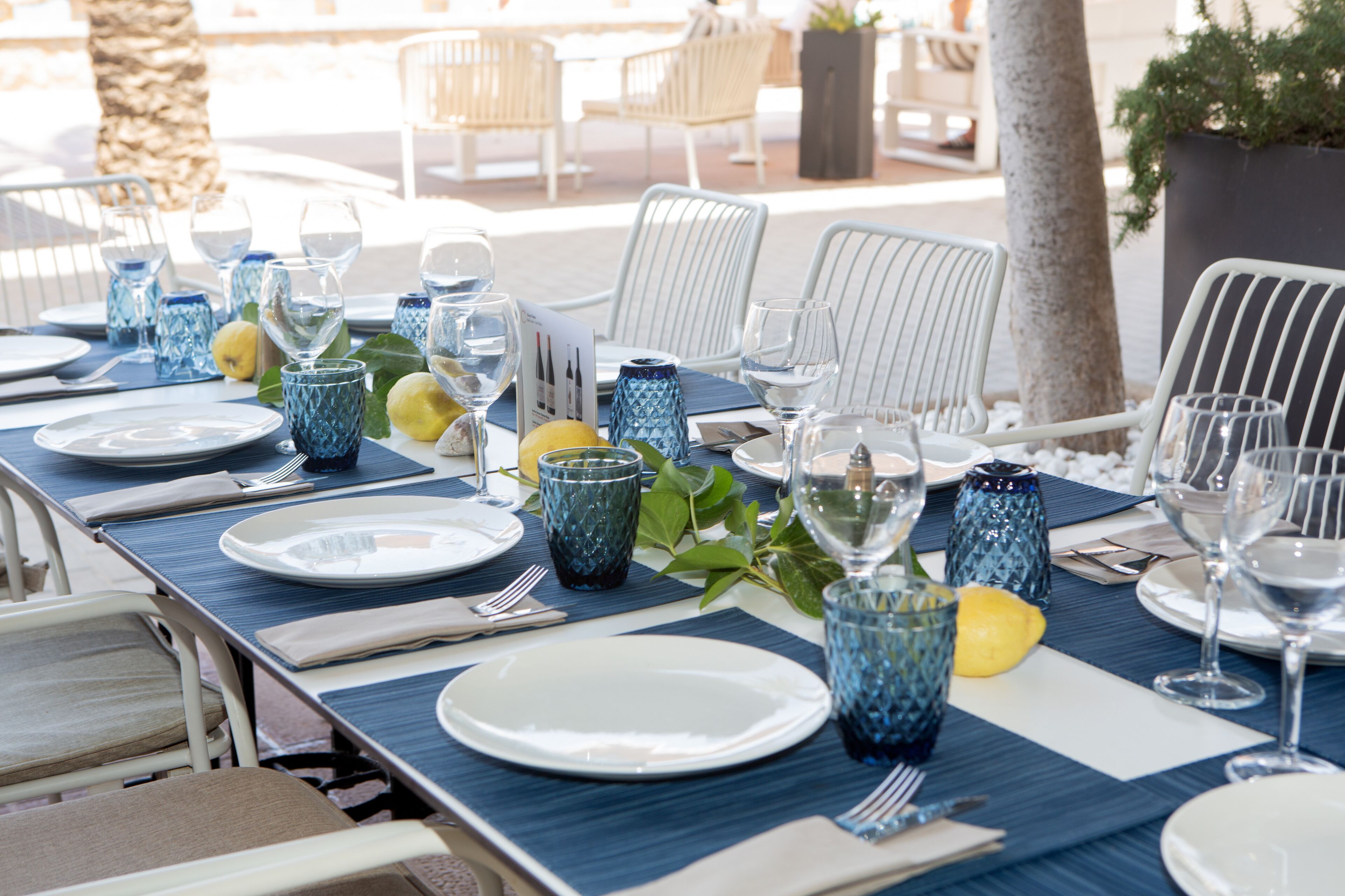 A table set for dining with blue placemats, white plates, and blue glassware.