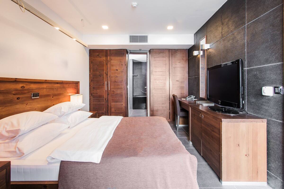 A modern hotel room with a large bed, wooden wardrobe, a TV, and a desk.