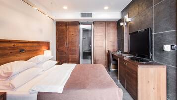 A modern hotel room with a large bed, wooden wardrobe, a TV, and a desk.