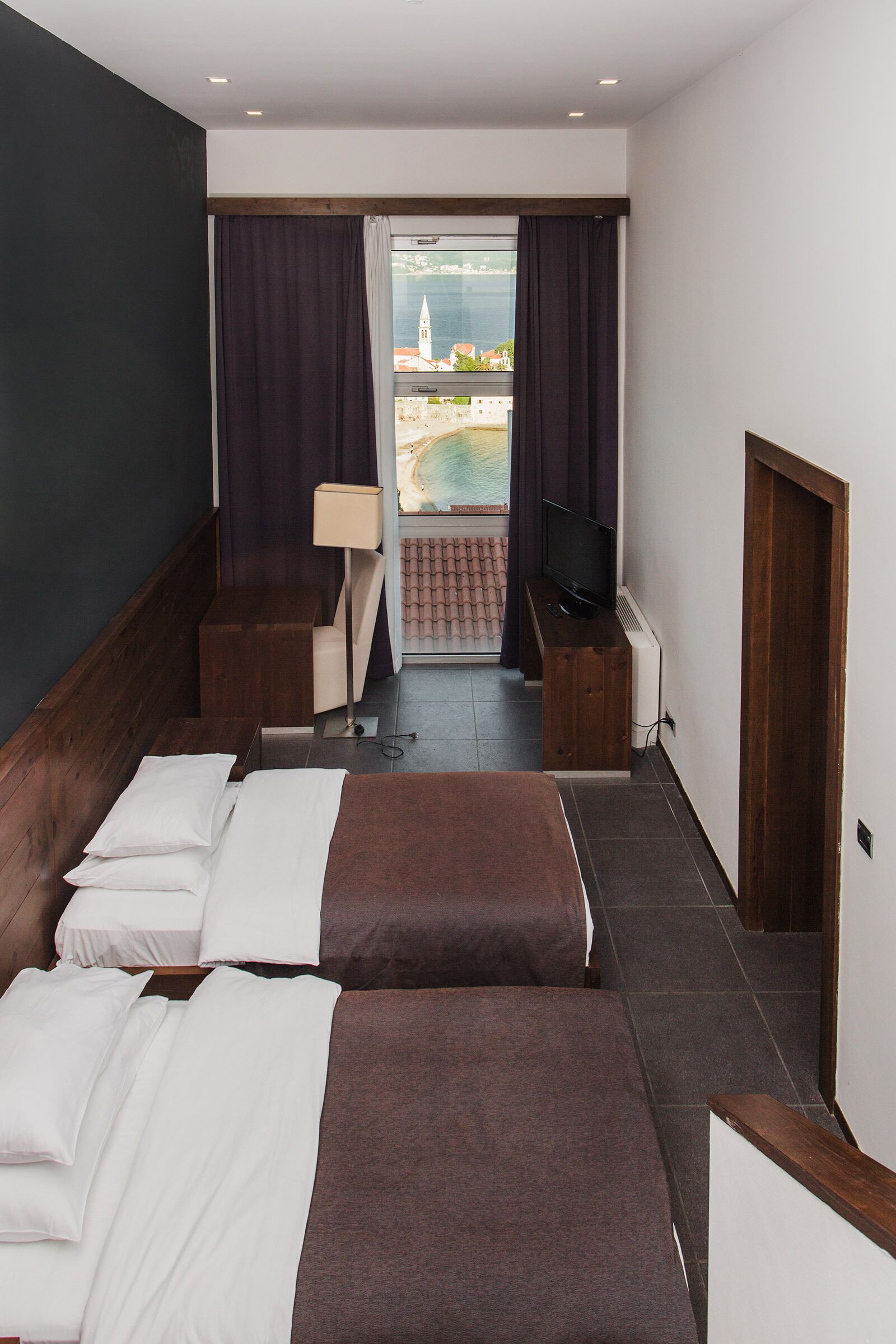 Habitación de hotel con dos camas, televisión, escritorio y vista al mar.