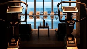 A gym with two treadmills, a small table with items, and a view of the sea through large windows. - Avala Resort & Villas (Budva)