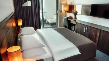Habitación de hotel con cama, lámpara de noche, escritorio, silla, televisor y vistas al exterior.
