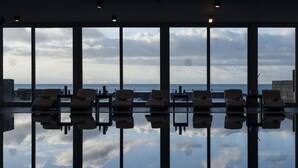 A room with large windows offering a view of the sea. There are several lounge chairs aligned in the room. - Avala Resort & Villas (Budva)
