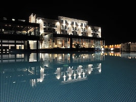 Vista nocturna de un hotel con una piscina que refleja la arquitectura del edificio.