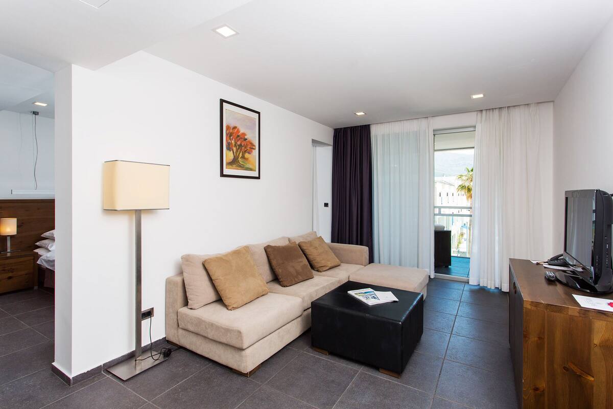 A modern living room with a beige sofa, a black coffee table, a TV on a wooden stand, and a painting on the wall.