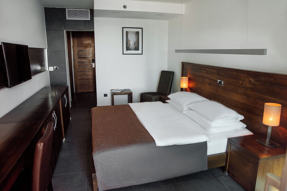 A hotel room with a bed, bedside table, lamp, chair, and a television on a stand.