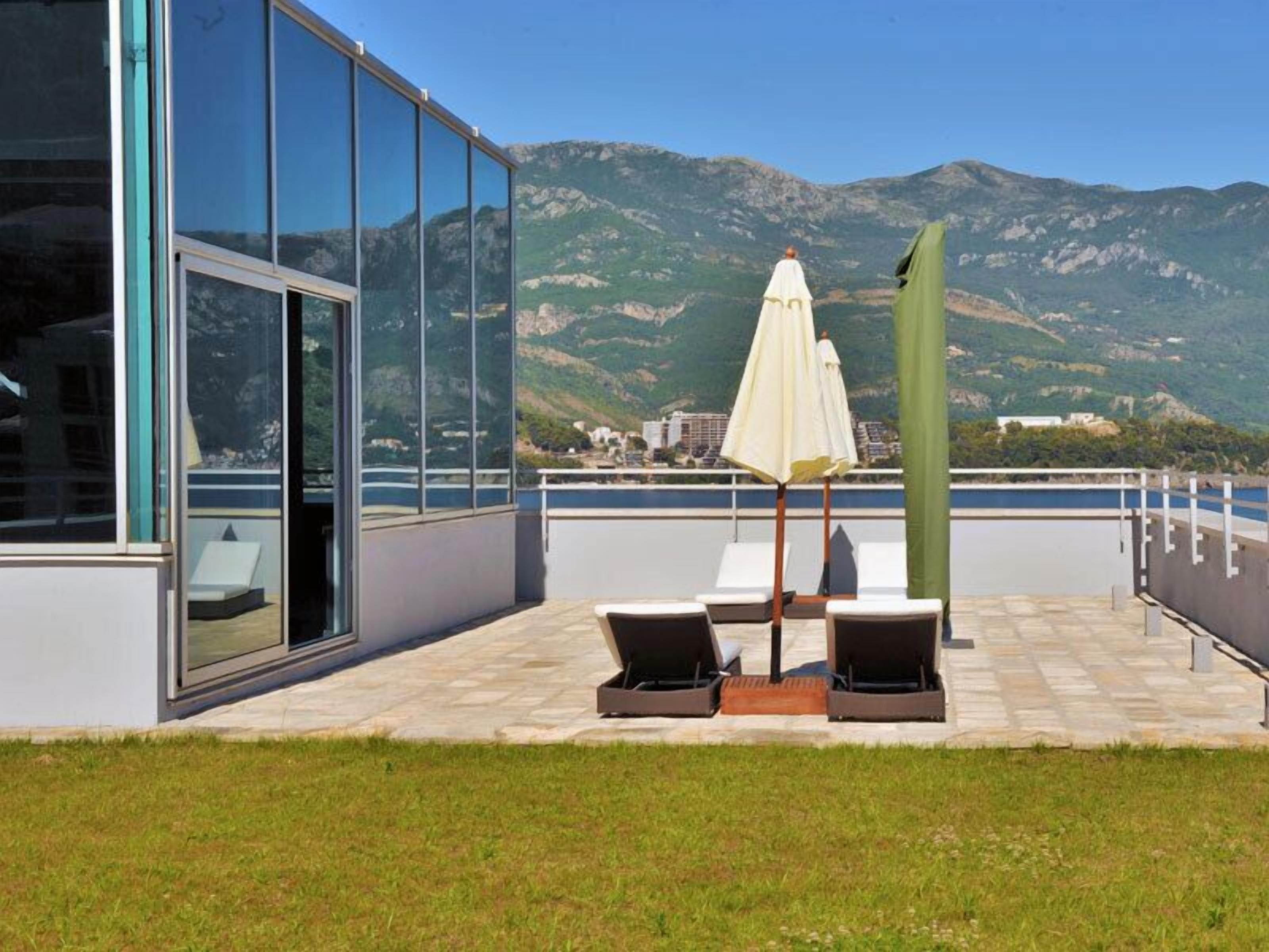 A terrace with lounge chairs and a table, overlooking a mountainous landscape.
