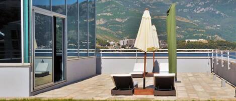 A terrace with lounge chairs and a table, overlooking a mountainous landscape.