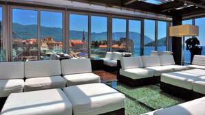 A modern interior with large windows offering views of a coastal town and mountains. - Avala Resort & Villas (Budva)