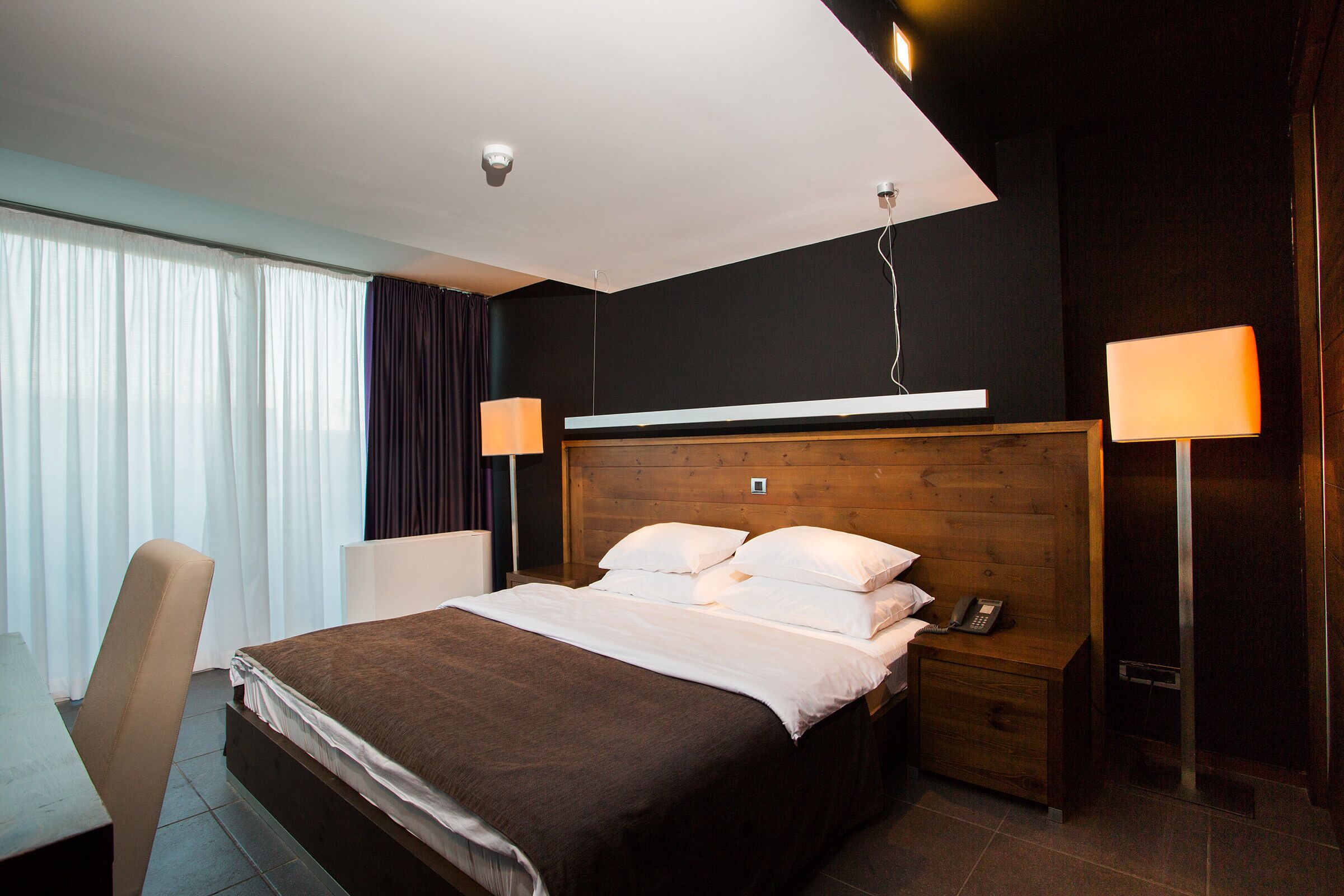 A hotel room with a bed, bedside table, lamp, and a chair.