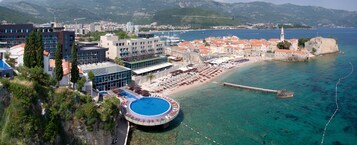 Un hotel costero con piscina, zona de playa y vistas al mar y a las montañas.