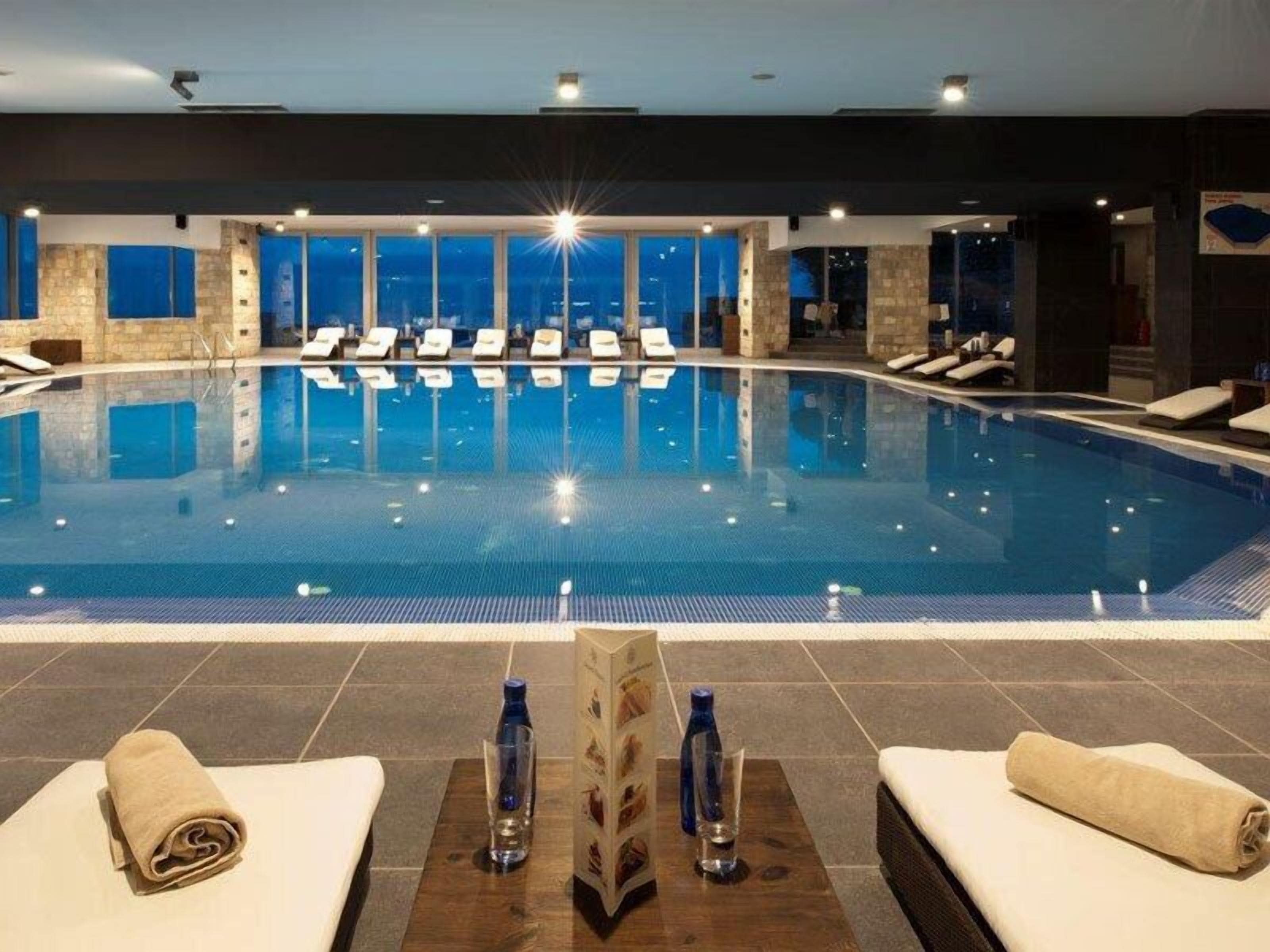 An indoor swimming pool with lounge chairs and a view of the city at night.