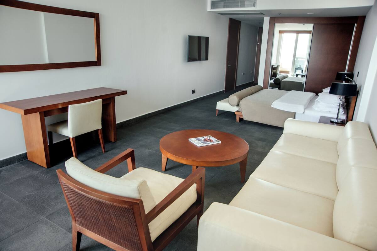 A modern hotel room with a sofa, armchair, and a small wooden table.