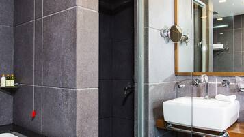 Un baño moderno con ducha de vidrio, un lavamanos blanco y un espejo grande.