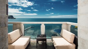 A balcony with two beige cushioned sofas, a small table, and a clear view of the ocean and a boat. - Avala Resort & Villas (Budva)